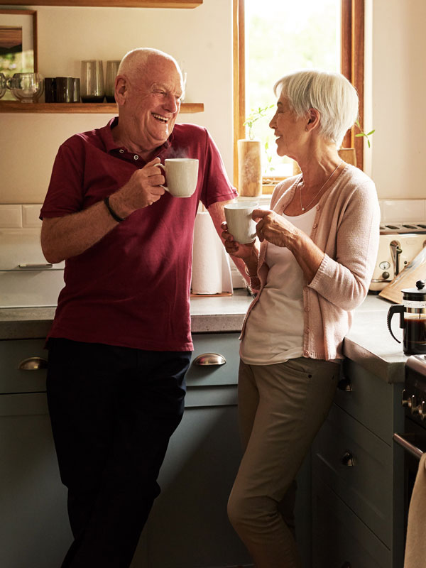 Senior couple in kitchen enjoying cups of coffee and laughing