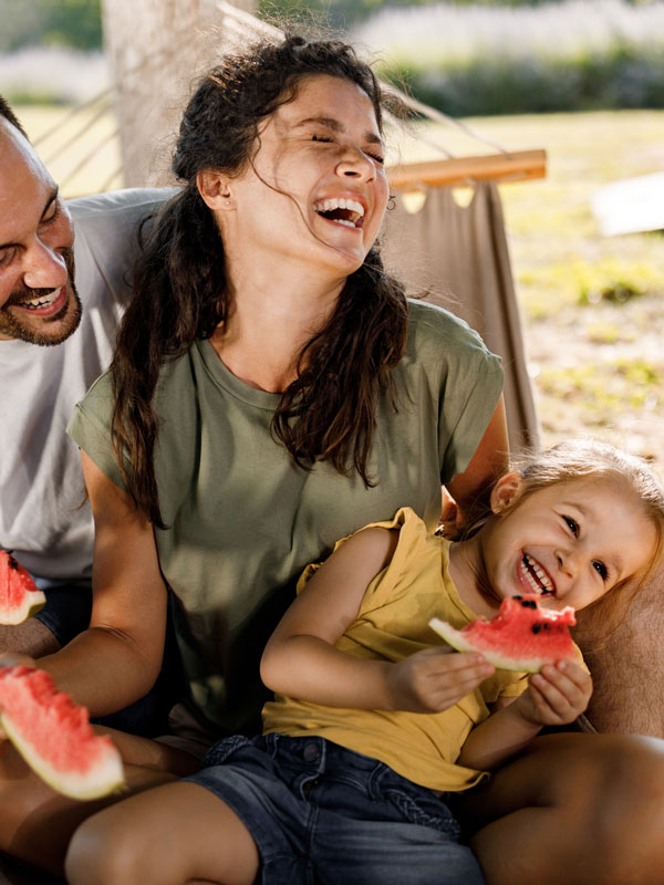 Cheerful parents and their small daughter having fun while eating watermelon